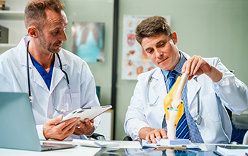In a hospital meeting room,Italian male and Caucasian male discuss medical cases at desk with X-ray films, blood samples, patient information, on diagnosing heart disease and treatment guidelines